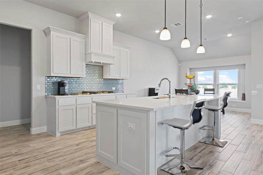 Kitchen with sink, decorative light fixtures, light wood-type flooring, a kitchen island with sink, and white cabinetry