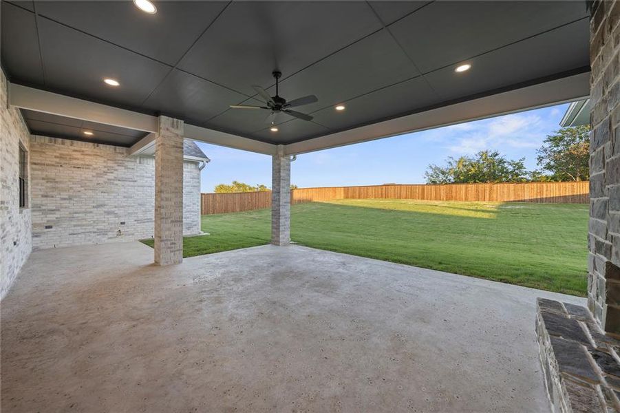 Covered patio with a concrete surface, featuring brick-clad support columns and a dark paneled ceiling with recessed lighting and a ceiling fan