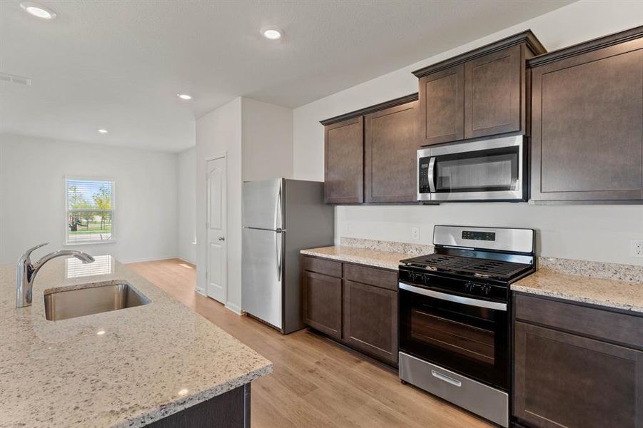 Kitchen featuring light wood-type flooring, appliances with stainless steel finishes, sink, and light stone countertops