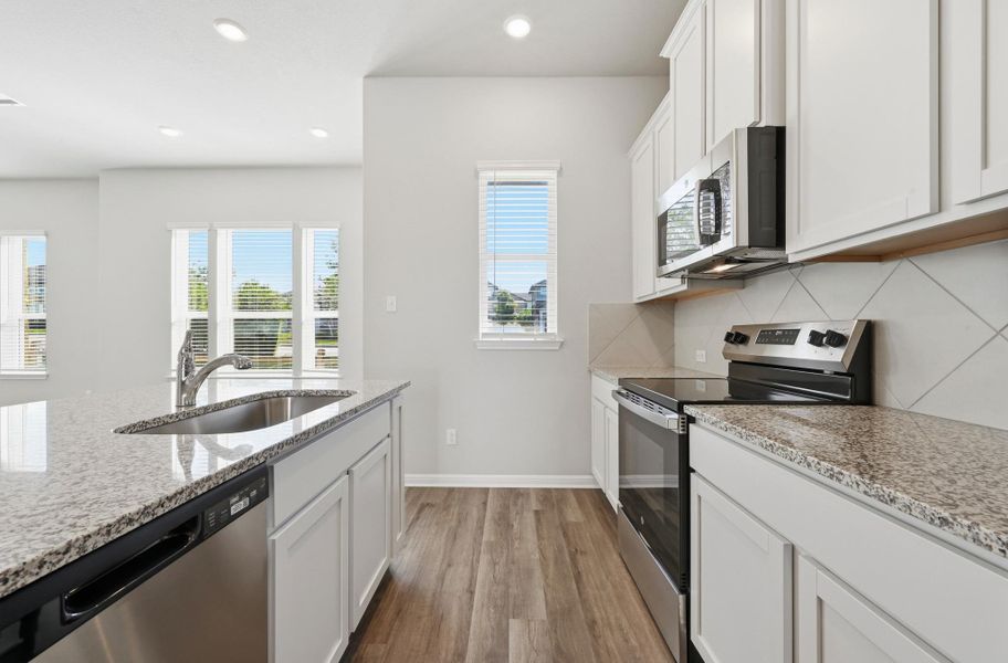 Kitchen featuring a stainless steel sink, granite countertops, wood-finish flooring, white cabinetry, and stainless steel appliances Kitchen featuring a stainless steel sink, granite countertops, wood-finish flooring, white cabinetry, and stainless steel appliances
