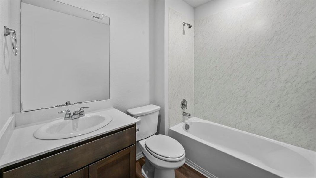 Full bathroom featuring a single vanity with an integrated sink, a large wall-mounted mirror, a toilet, and a bathtub with a shower and patterned shower surround