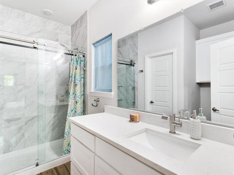 Bathroom featuring a spacious vanity with an undermount sink, a large mirror, white cabinetry, a window with frosted glass, and a tub with a sliding glass door and tile surround