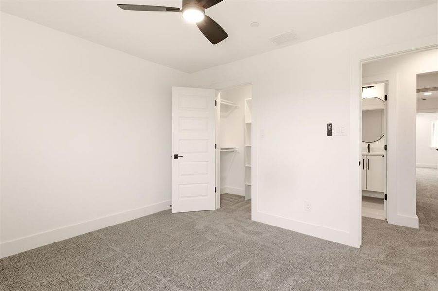 Unfurnished bedroom with carpet flooring, a spacious closet, a ceiling fan, and connected bathroom