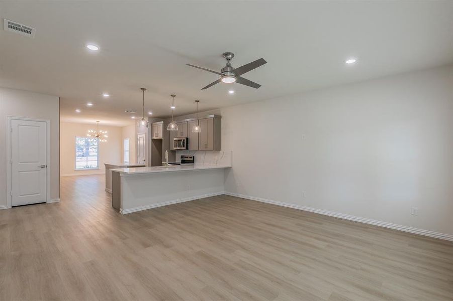 Kitchen featuring ceiling fan with notable chandelier, light hardwood / wood-style flooring, gray cabinets, kitchen peninsula, and stainless steel appliances