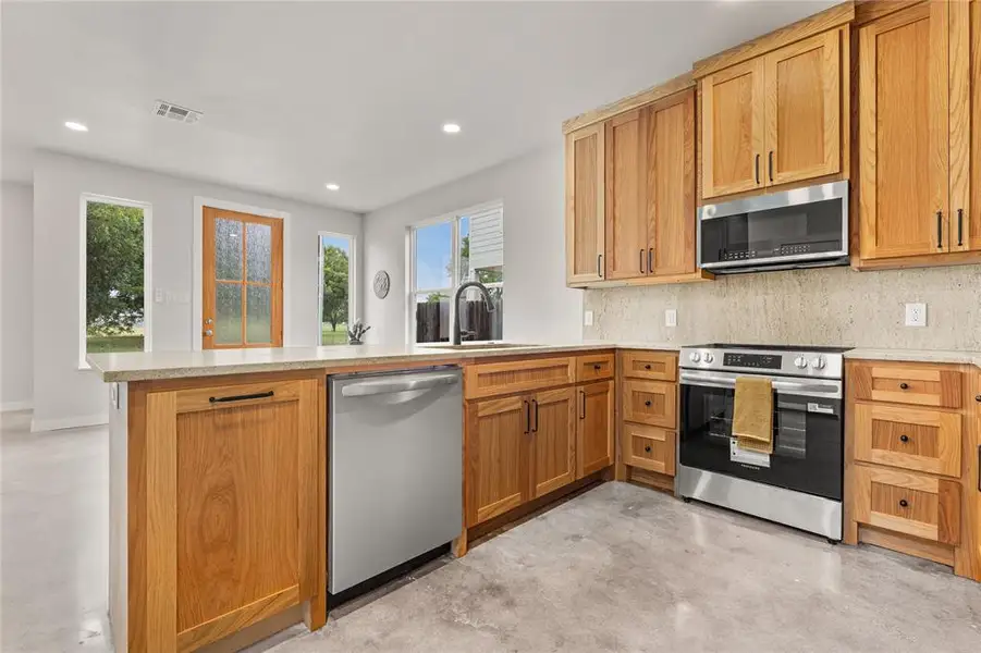 Kitchen with concrete floors, a peninsula, stainless steel appliances, tasteful backsplash, and brown cabinets Kitchen with concrete floors, a peninsula, stainless steel appliances, tasteful backsplash, and brown cabinets