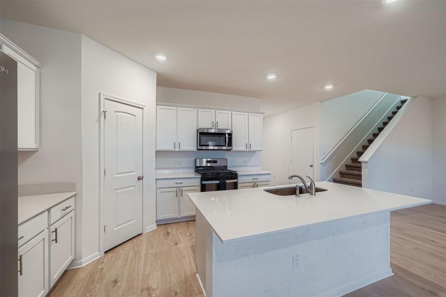 Kitchen with stainless steel appliances, white cabinetry, a center island with sink, light wood-type flooring, and recessed lighting
