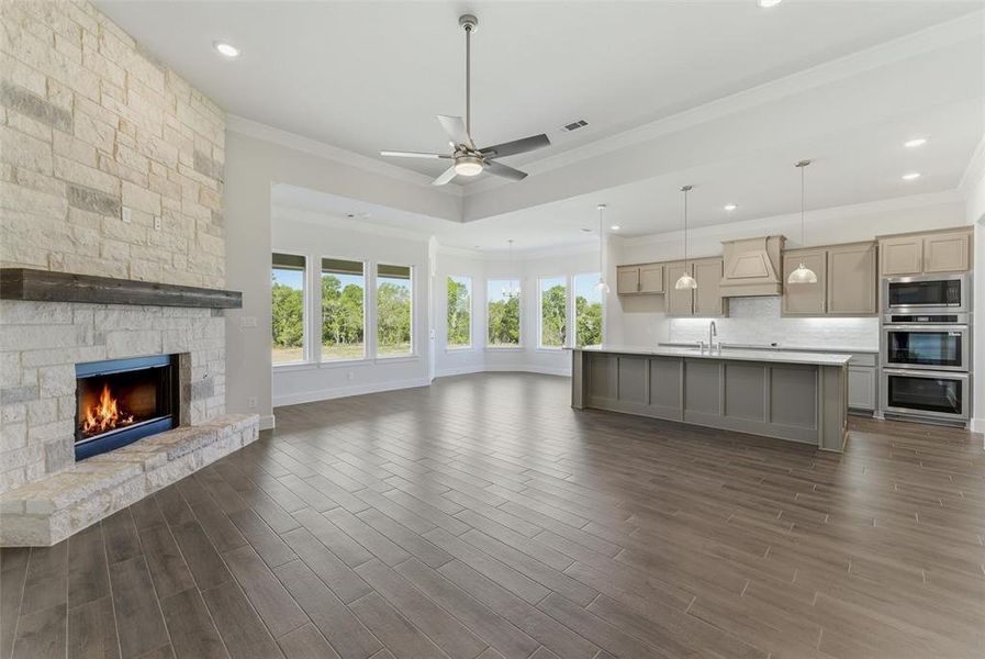 Unfurnished living room with a fireplace, a ceiling fan, wood tiled floors, and ornamental molding