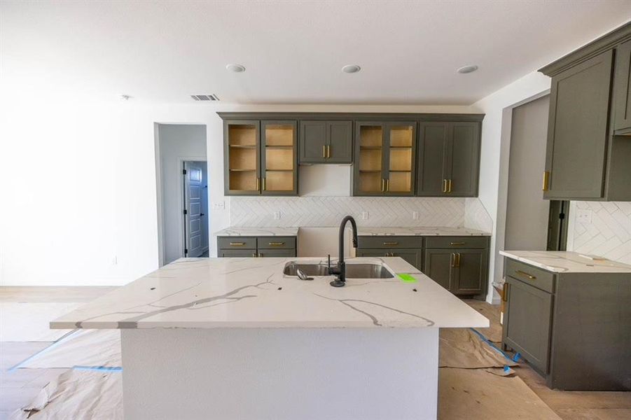 Kitchen featuring a center island with sink, sink, light stone counters, and backsplash