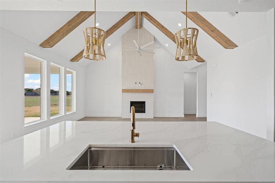 Kitchen featuring light stone countertops, sink, beamed ceiling, pendant lighting, and a fireplace