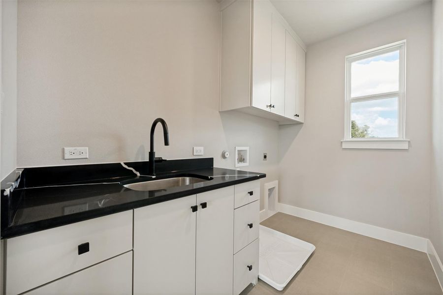 Functional laundry space featuring a sink, dark countertops, and ample cabinetry for storage. Functional laundry space featuring a sink, dark countertops, and ample cabinetry for storage.