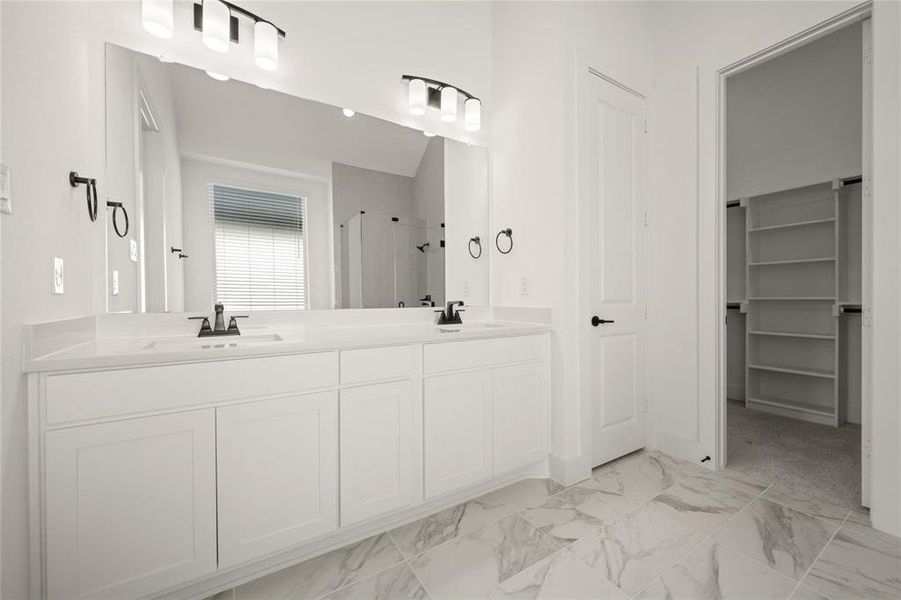 Bathroom with double vanity, a shower stall, light marble finish flooring, and a walk in closet