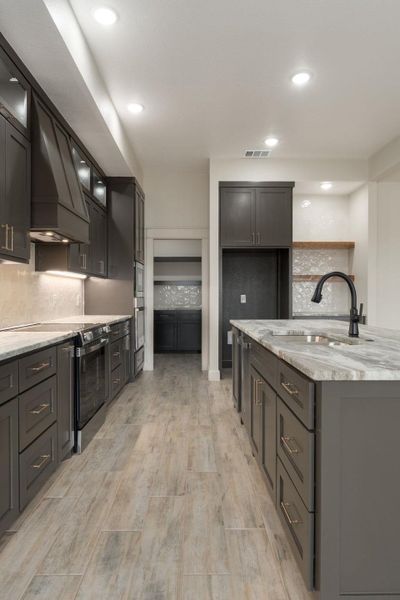 Kitchen with tasteful backsplash, stainless steel electric range, light stone countertops, custom range hood, and light wood-style flooring