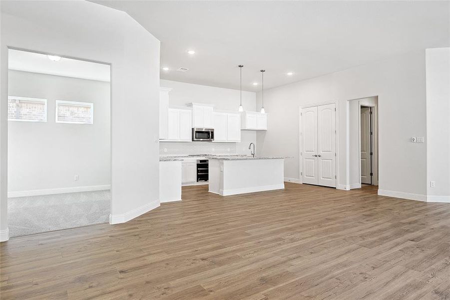 Kitchen with open floor plan, light wood-style flooring, white cabinets, pendant lighting, and a kitchen island with sink