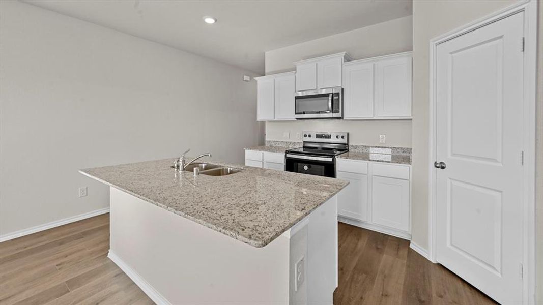 Kitchen featuring stainless steel appliances, white cabinets, an island with sink, dark wood finished floors, and light stone counters