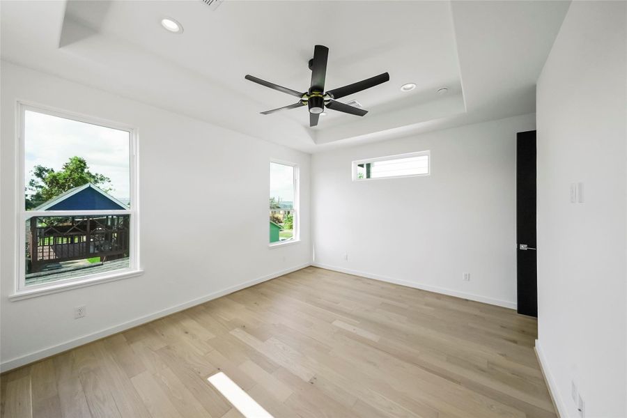 A bright, modern room with expansive windows, light hardwood floors, and high ceilings featuring recessed lighting and a ceiling fan. Enjoy serene views of outdoor greenery. A bright, modern room with expansive windows, light hardwood floors, and high ceilings featuring recessed lighting and a ceiling fan. Enjoy serene views of outdoor greenery.