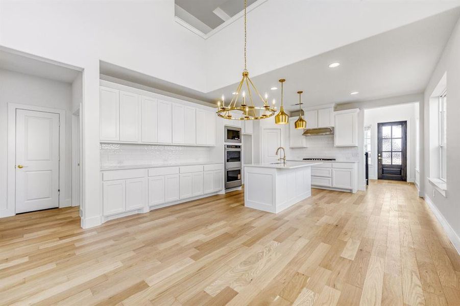 Kitchen featuring hanging lights, white cabinetry, decorative backsplash, light wood finished floors, and a kitchen island with sink
