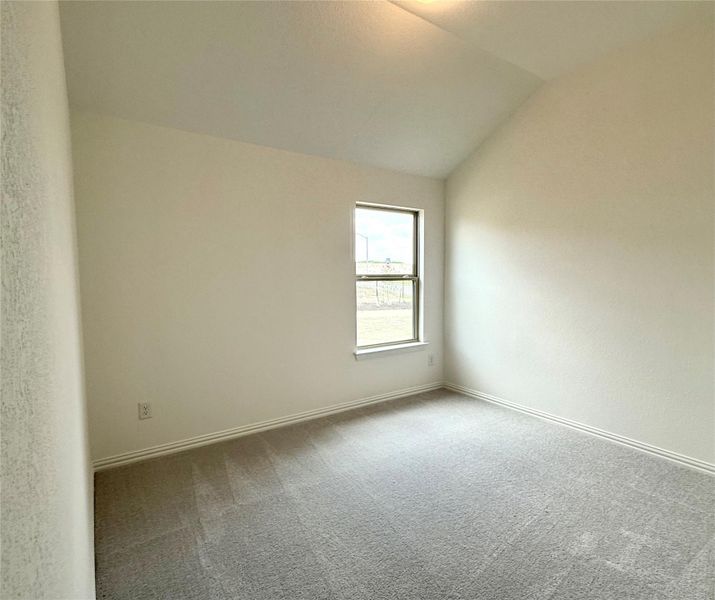 Carpeted empty room with vaulted ceiling and baseboards Carpeted empty room with vaulted ceiling and baseboards