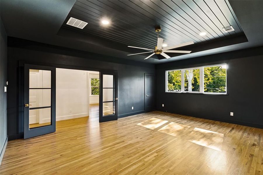 Spacious room featuring wood-finish flooring, a tray ceiling with recessed lighting, and a multi-pane window Spacious room featuring wood-finish flooring, a tray ceiling with recessed lighting, and a multi-pane window