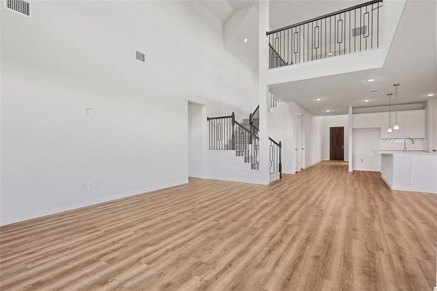 Unfurnished living room featuring light hardwood / wood-style flooring, a towering ceiling, and sink