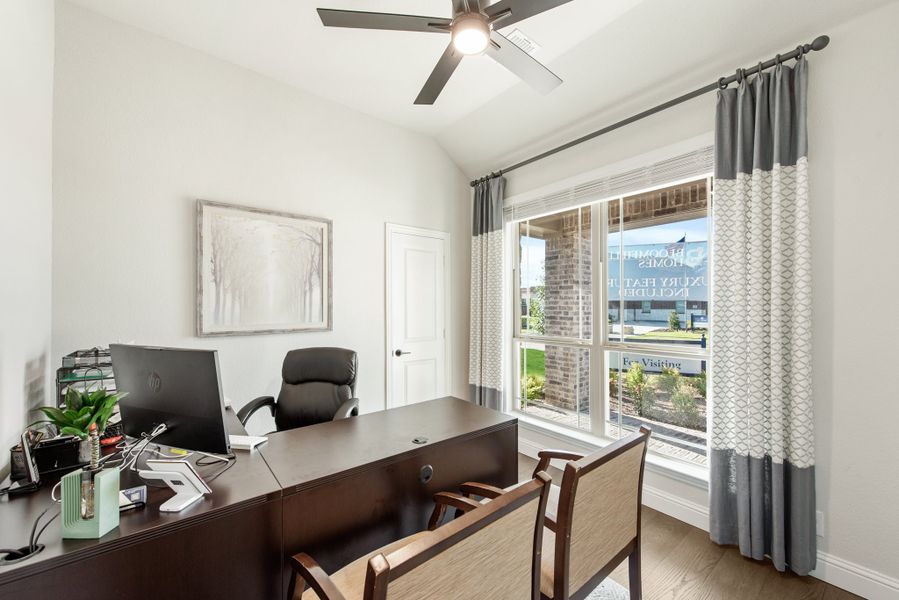Home office with dark wood desk, computer, ceiling fan, and large window with gray curtains