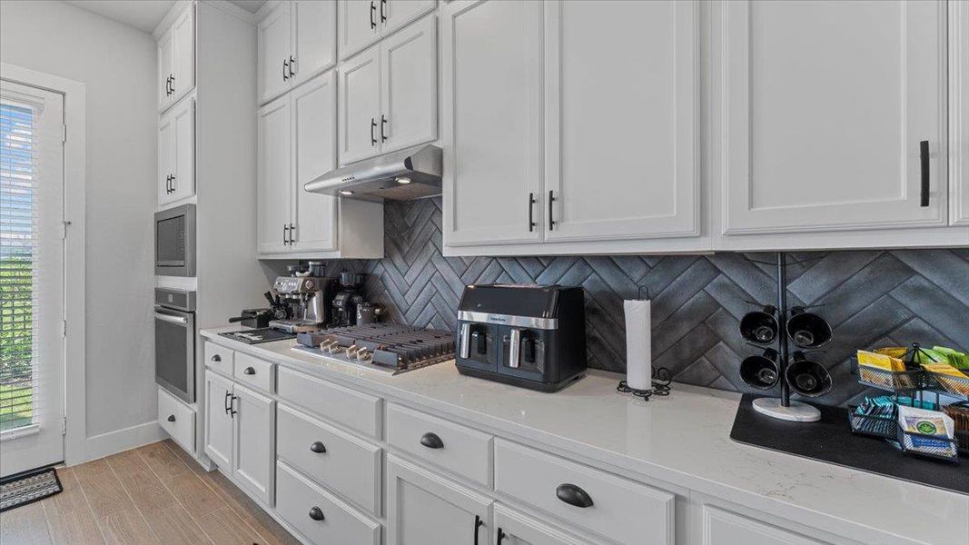 Kitchen featuring white cabinets, tasteful backsplash, light wood-type flooring, stainless steel appliances, and light stone countertops Kitchen featuring white cabinets, tasteful backsplash, light wood-type flooring, stainless steel appliances, and light stone countertops