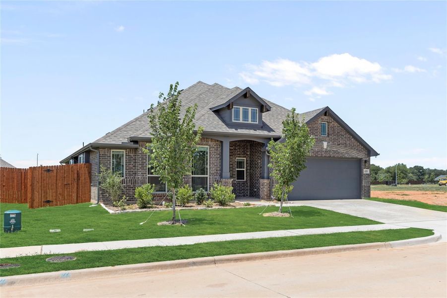 Single-story brick home with arched entry, two-car garage, and landscaped front yard with young trees