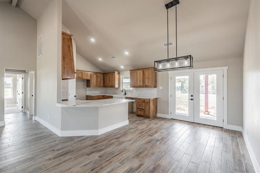 Kitchen with high vaulted ceiling, brown cabinetry, a peninsula, tasteful backsplash, and light wood finished floors Kitchen with high vaulted ceiling, brown cabinetry, a peninsula, tasteful backsplash, and light wood finished floors