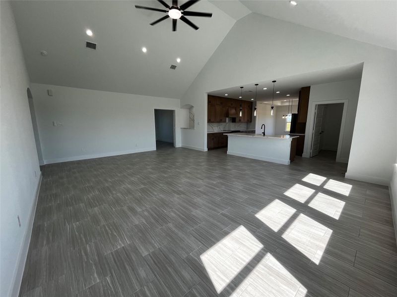 This spacious, open-concept living area features high ceilings, modern tile flooring, and ample natural light. The kitchen boasts a stylish island with pendant lighting, wood cabinets, and a sleek faucet. Ideal for entertaining.