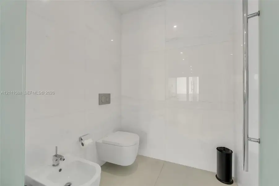 Wall-to-wall large-format porcelain tile, wall-mounted dual-flush toilet, pedestal bidet with chrome fixtures, and a vertical chrome towel warmer Wall-to-wall large-format porcelain tile, wall-mounted dual-flush toilet, pedestal bidet with chrome fixtures, and a vertical chrome towel warmer