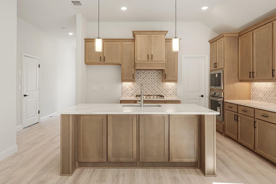 Kitchen with large center island, light wood cabinets, white quartz countertops, and patterned tile backsplash