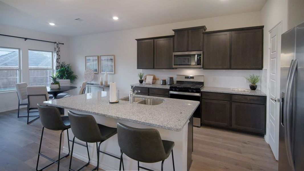 Kitchen featuring an island with a double basin sink and integrated breakfast bar, dark wood-finish cabinetry, stainless steel appliances, and a white tile backsplash Kitchen featuring an island with a double basin sink and integrated breakfast bar, dark wood-finish cabinetry, stainless steel appliances, and a white tile backsplash