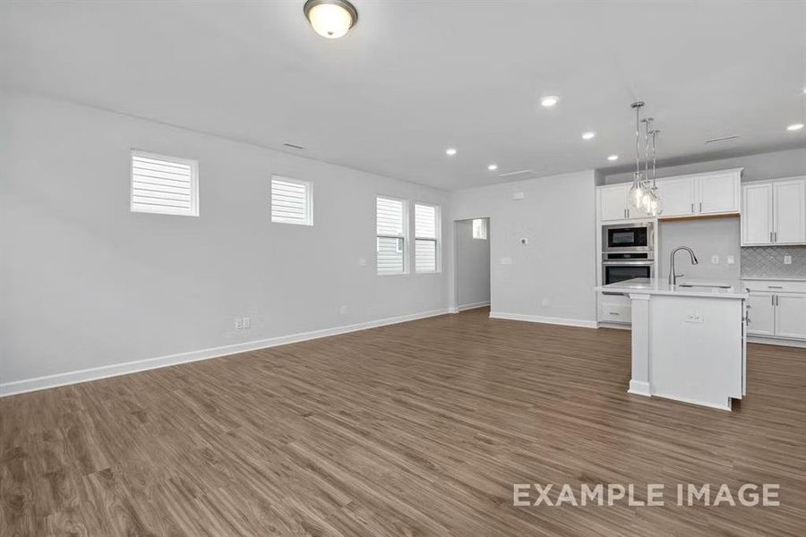 Kitchen with tasteful backsplash, stainless steel oven, hanging light fixtures, black microwave, and a kitchen island with sink