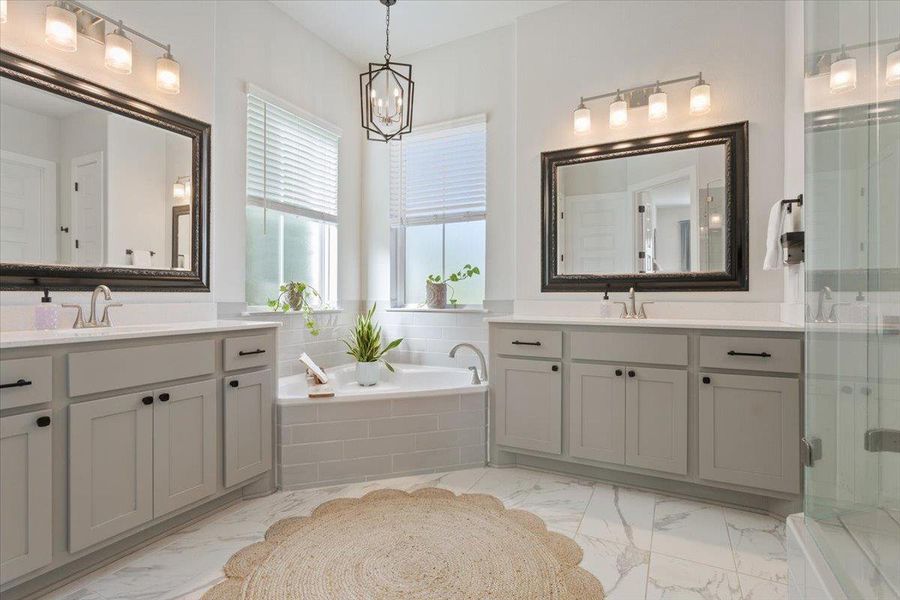 Full bath with a bath, two vanities, a shower stall, and suspended lighting