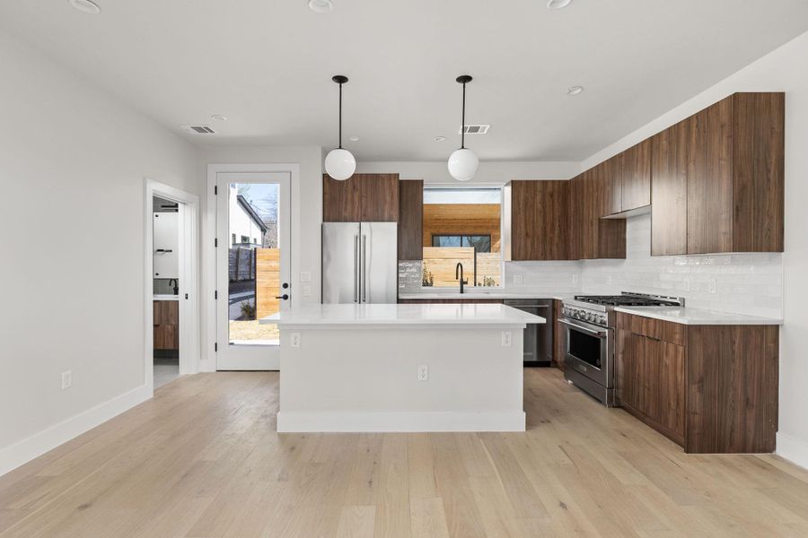 Kitchen featuring light wood-type flooring, premium appliances, a center island, and light countertops