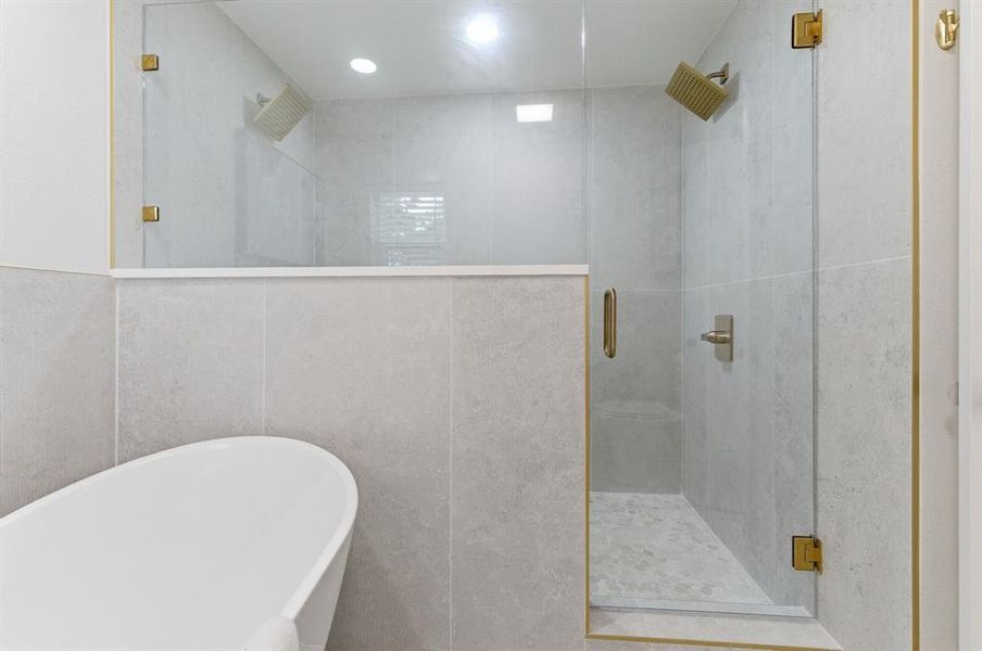 Bathroom featuring a freestanding bathtub, a walk-in shower with glass doors, and dual showerheads Bathroom featuring a freestanding bathtub, a walk-in shower with glass doors, and dual showerheads