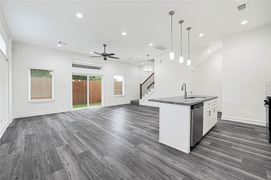 This modern, open-concept living space features sleek gray flooring, a stylish kitchen island with pendant lighting, and ample natural light from large windows and sliding glass doors leading to a fenced backyard. Perfect for entertaining and family living. This modern, open-concept living space features sleek gray flooring, a stylish kitchen island with pendant lighting, and ample natural light from large windows and sliding glass doors leading to a fenced backyard. Perfect for entertaining and family living.