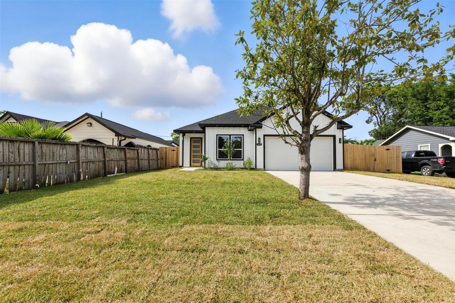 Charming single-story home with modern design, featuring a spacious front yard and a well-maintained lawn. The property includes a two-car garage and a welcoming path leading to the entrance, surrounded by a wooden fence for added privacy.