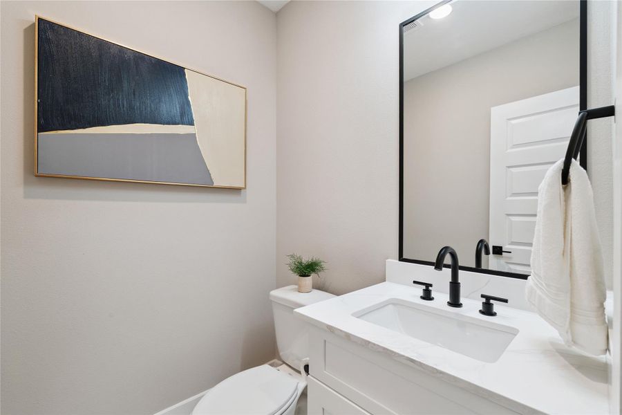 The powder room delivers quiet contrast—matte black fixtures set against soft stone textures and sculptural lighting.