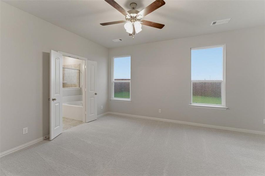 Spacious room featuring light gray carpeting, two windows with white trim, and a ceiling fan with wood-finish blades Spacious room featuring light gray carpeting, two windows with white trim, and a ceiling fan with wood-finish blades