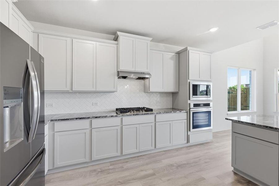 Kitchen featuring stainless steel appliances, light stone countertops, light wood-type flooring, recessed lighting, and white cabinets Kitchen featuring stainless steel appliances, light stone countertops, light wood-type flooring, recessed lighting, and white cabinets