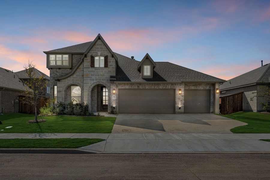 Two-story brick and stone home with three-car garage, arched entry, and manicured front lawn at dusk