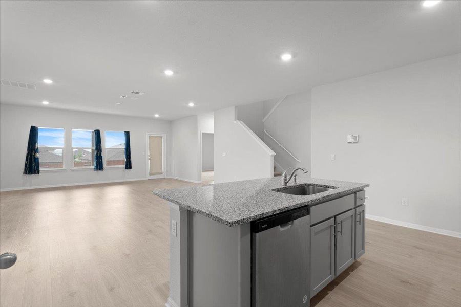 Kitchen island featuring a stainless steel sink and dishwasher, granite countertop, and gray cabinetry