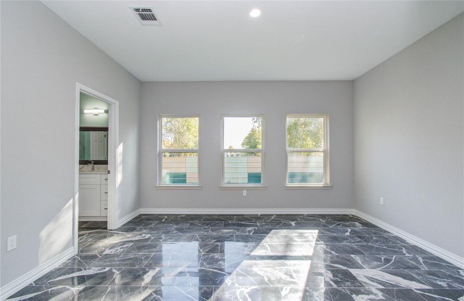 Bright room with large windows and sleek black marble flooring. Adjacent to a bathroom with modern fixtures. Neutral gray walls enhance the spacious feel.