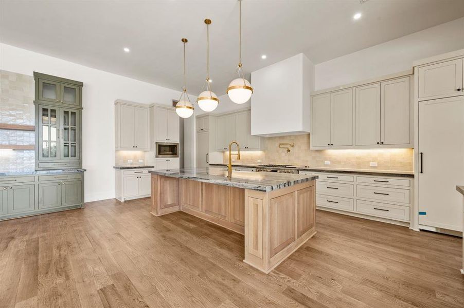 Dual tone kitchen with dark stone countertops, pendant lighting, tasteful backsplash, a kitchen island with sink, and built in appliances