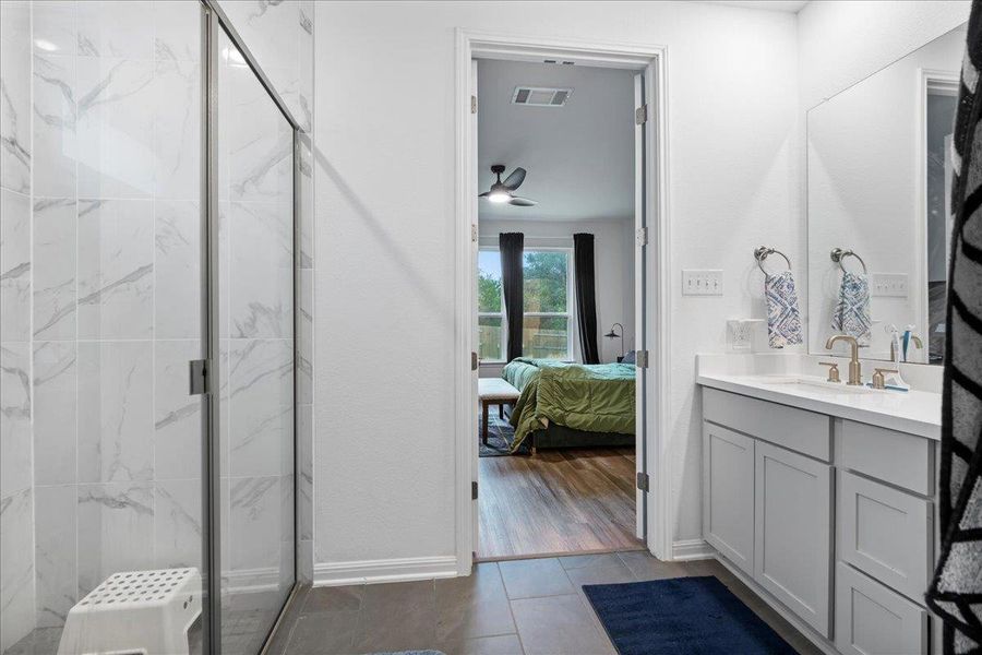 Ensuite bathroom featuring vanity, a marble finish shower, dark tile patterned flooring, and a ceiling fan