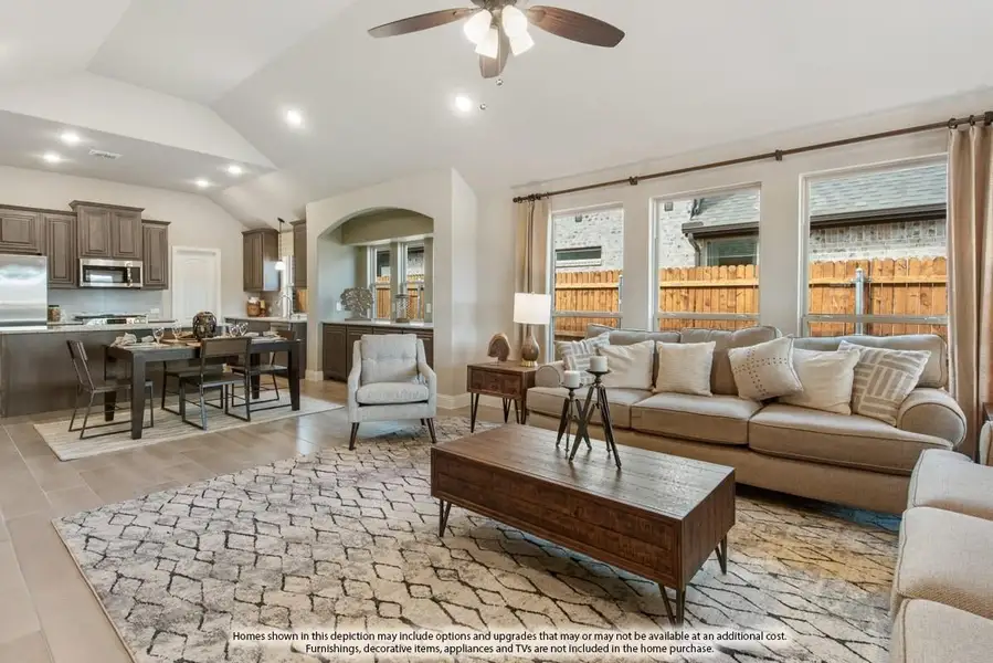 Open-concept living room with vaulted ceiling, ceiling fan, and view into kitchen and dining area