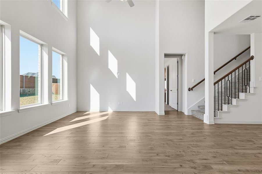 Unfurnished living room with stairway, light wood-style floors, healthy amount of natural light, a towering ceiling, and a ceiling fan