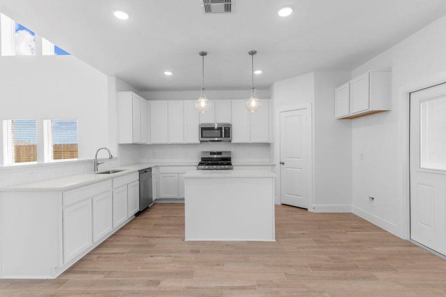 Bright and airy gourmet kitchen featuring tall white shaker cabinets, stainless steel appliances, island, and subway glass tile backsplash. **Image Representative of Plan Only and May Vary as Built**.