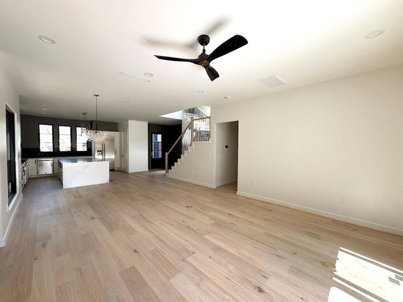 Unfurnished living room featuring ceiling fan with notable chandelier, light wood-type flooring, stairs, and baseboards