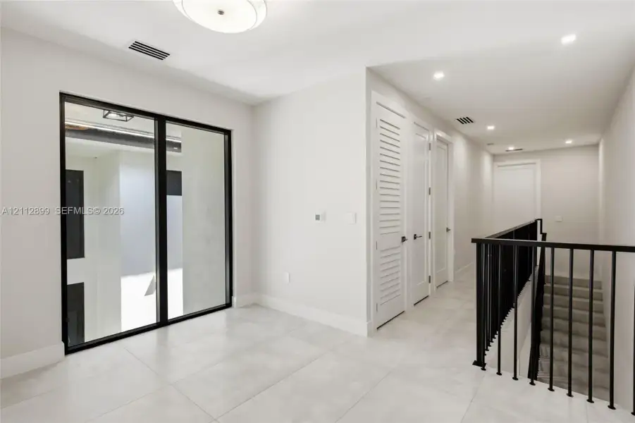 Large-format tile flooring, black-framed floor-to-ceiling glass window, recessed lighting, and a staircase with a black metal railing